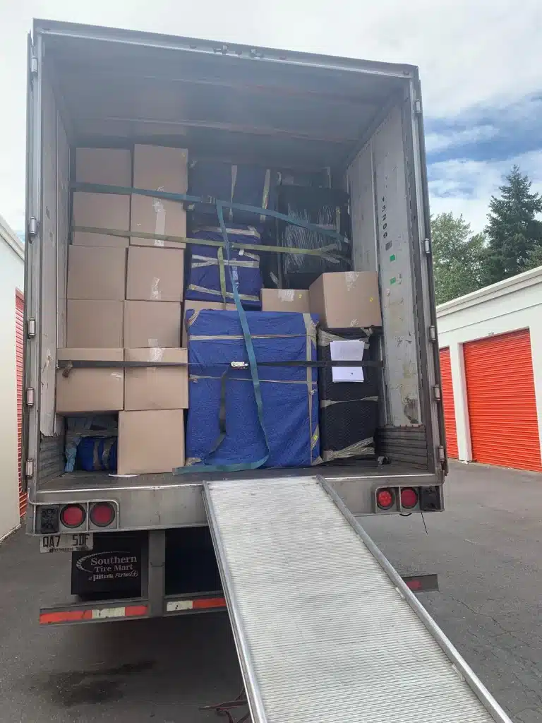 Neatly packed moving truck filled with labeled U-Haul boxes, bags, and wrapped furniture secured with a yellow strap.