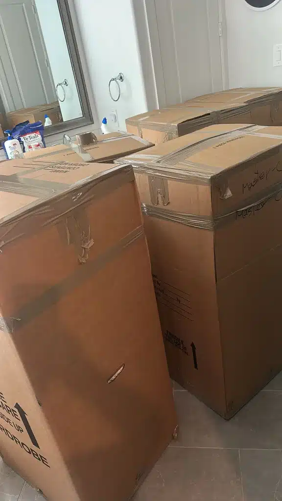 Sealed moving boxes labeled for the master closet stacked in a bathroom near a mirror and sink.