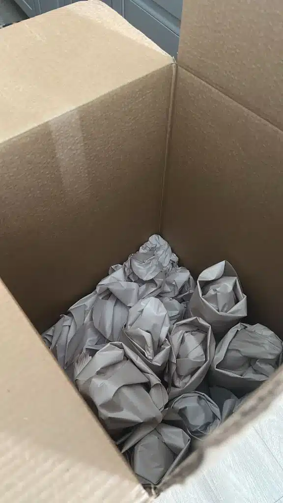 Open cardboard box filled with wrapped kitchen items in packing paper for moving or storage.