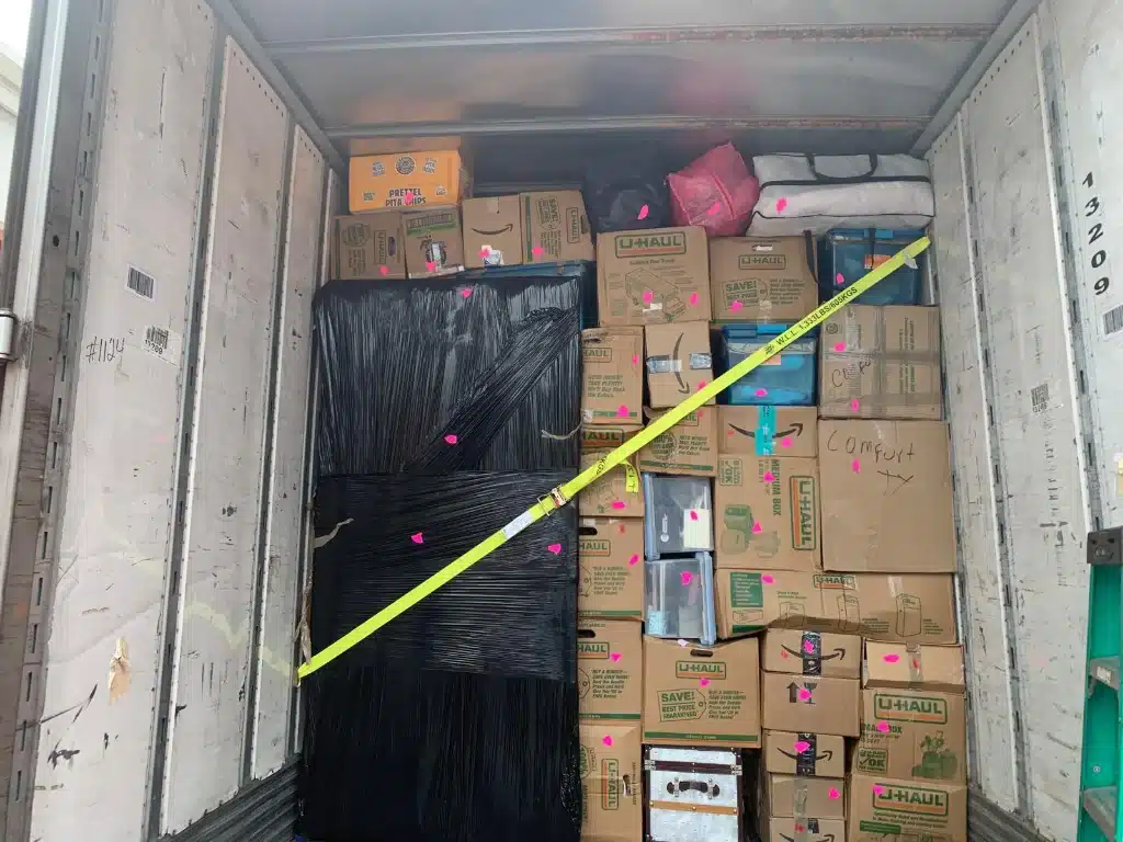 Neatly packed moving truck filled with labeled U-Haul boxes, bags, and wrapped furniture secured with a yellow strap.